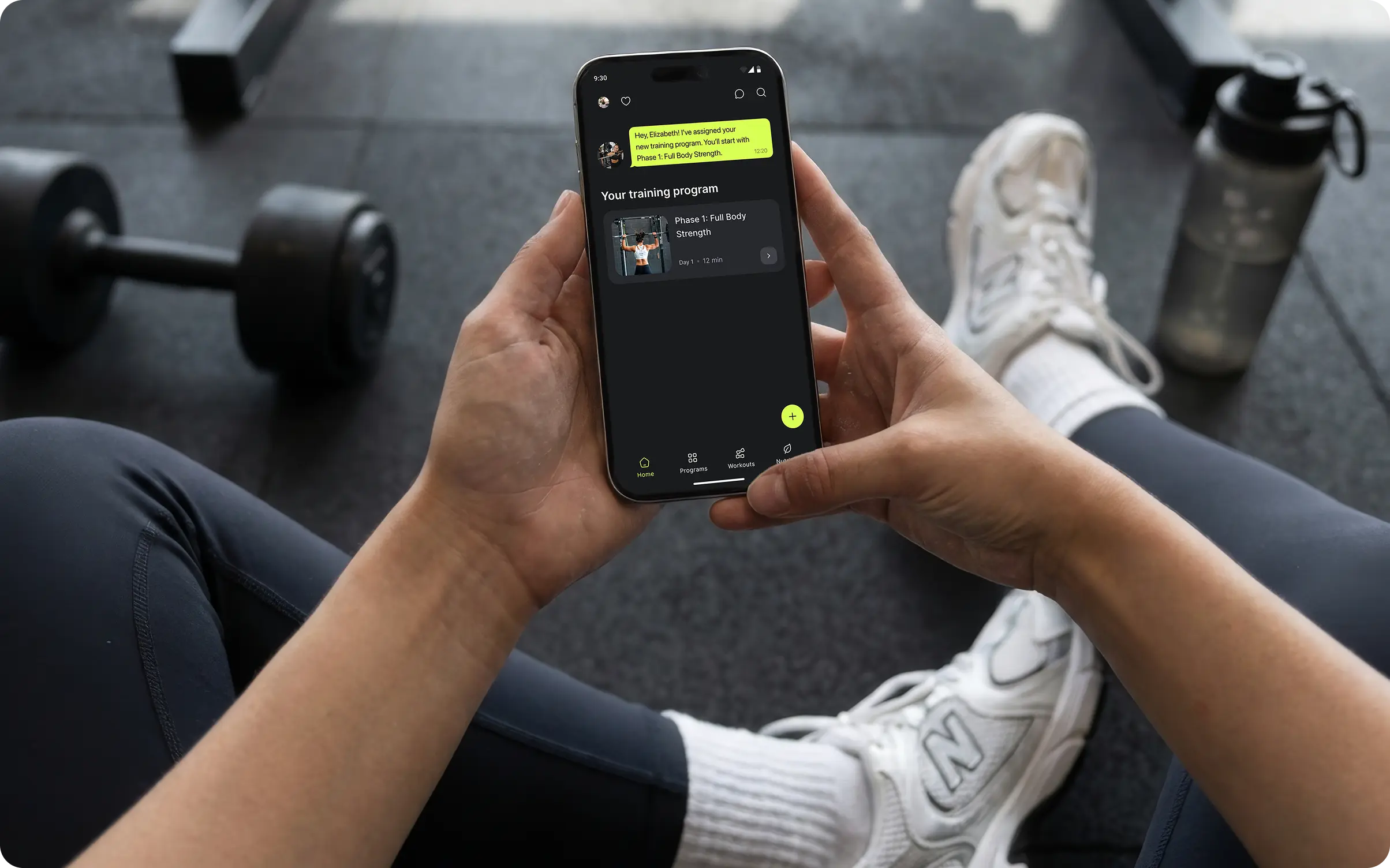 Person in a gym viewing assigned training program and coach message in Ymove fitness app on iPhone